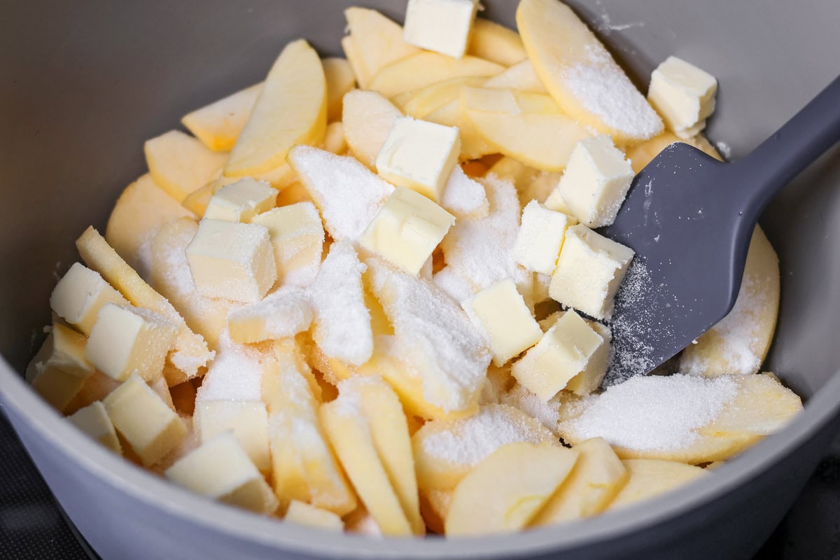 Sour cream apple pie elevates the classic with a rich, tangy, and creamy custard and a buttery crumb topping! Sliced apples, butter, and sugar in a pot.
