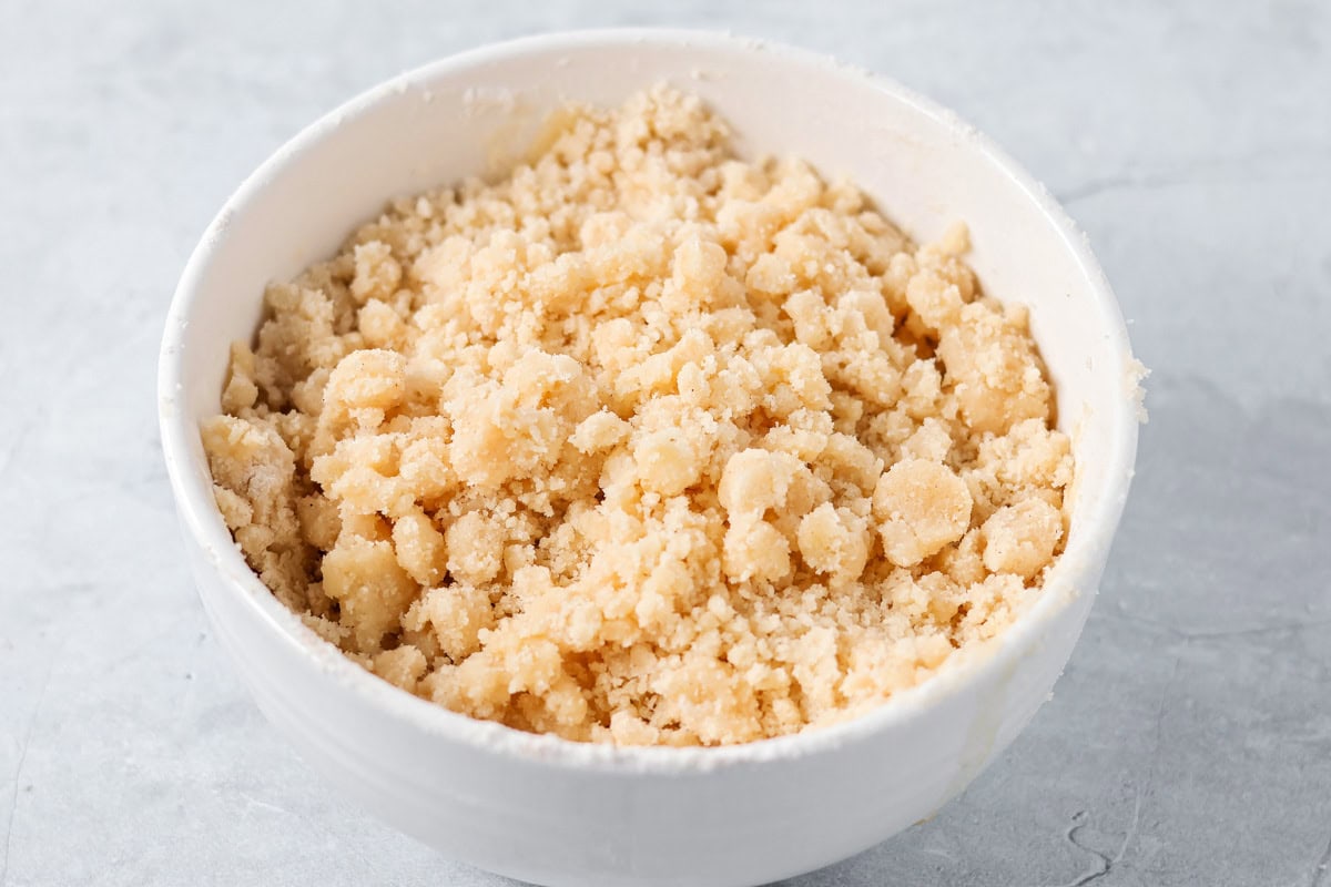 Sour cream apple pie elevates the classic with a rich, tangy, and creamy custard and a buttery crumb topping! Crumb topping in a white bowl.