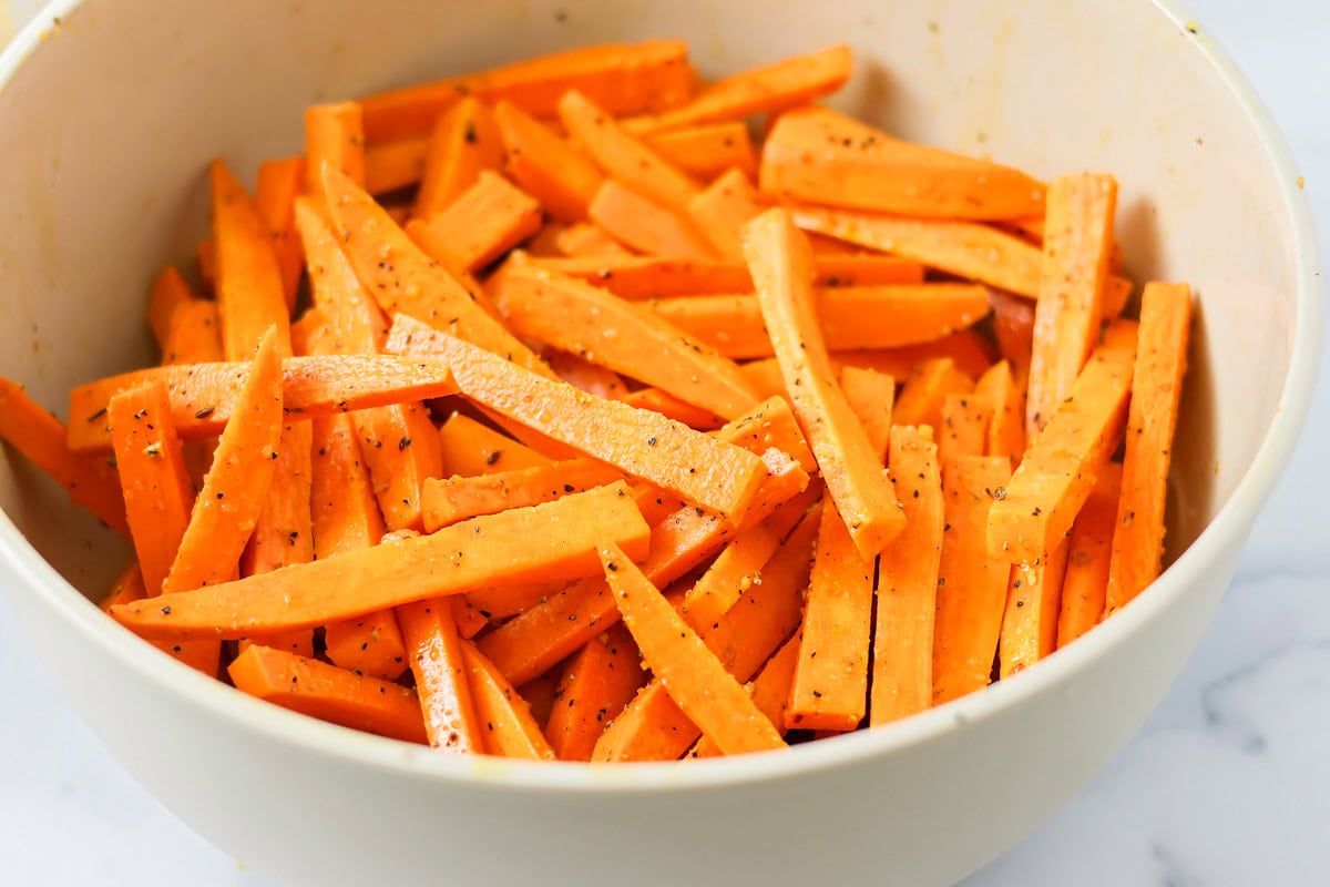Adding seasoning to cut sweet potatoes.