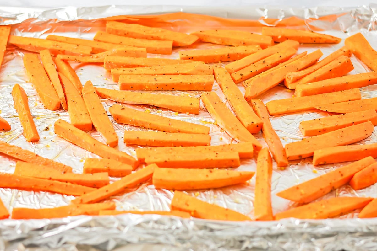 Seasoned sweet potatoes on a lined baking sheet.