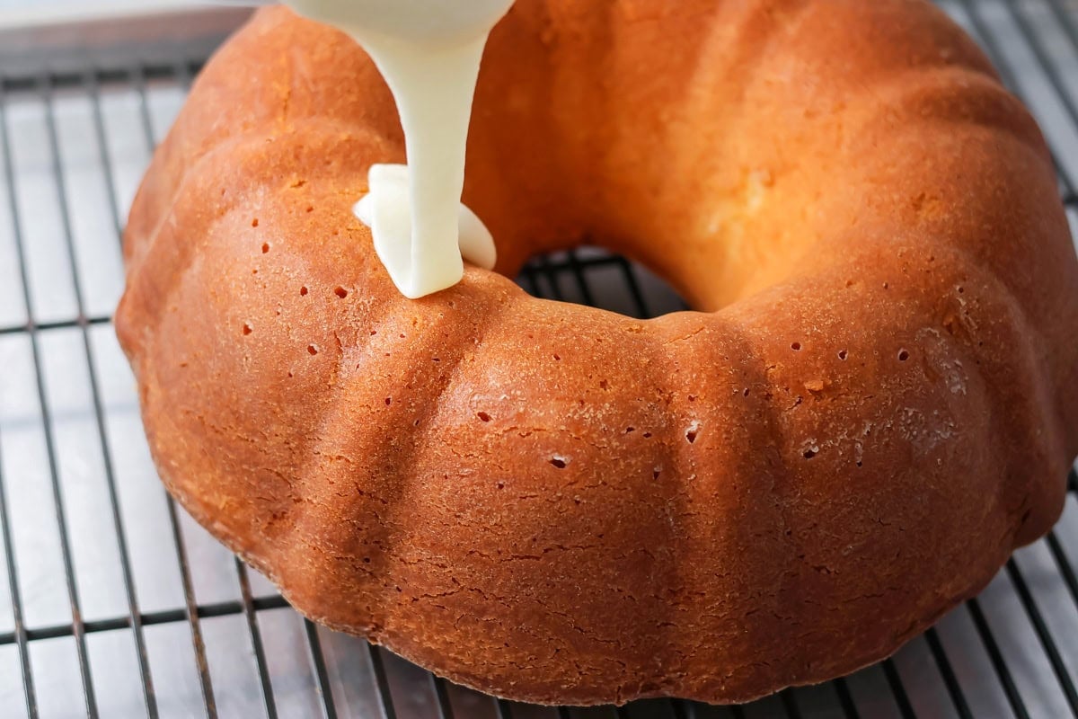 Glaze being poured on a baked bundt cake on a wire rack.
