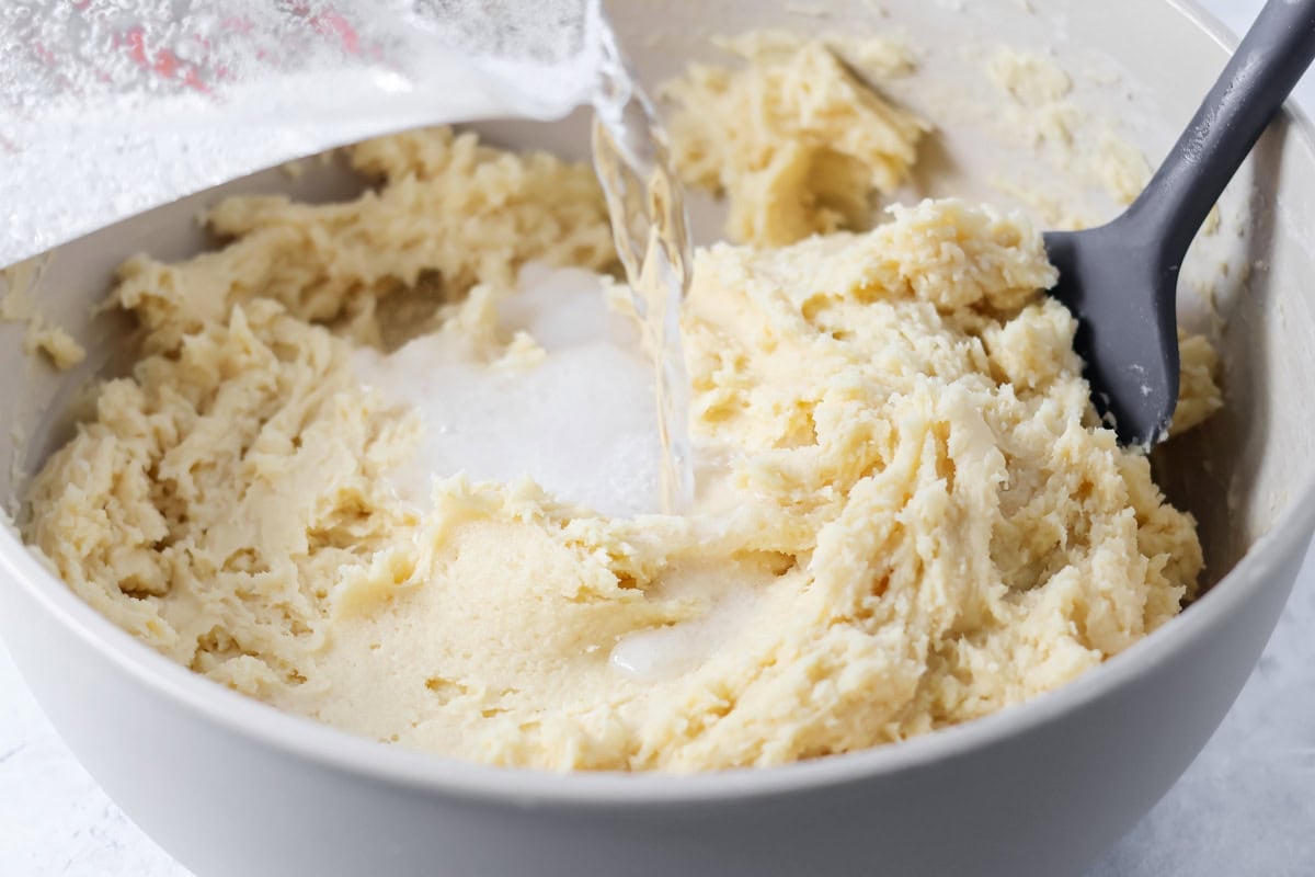 Pouring lemon lime soda into thick cake batter in a bowl.