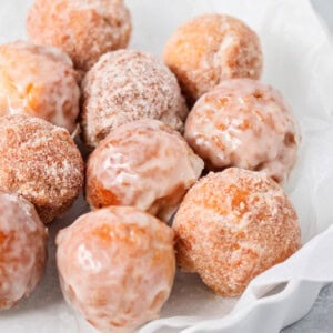 Glazed bonuts and sugared bonuts in dish lined with parchment paper.