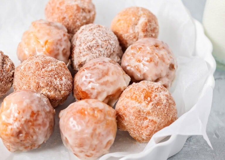 Glazed bonuts and sugared bonuts in dish lined with parchment paper.