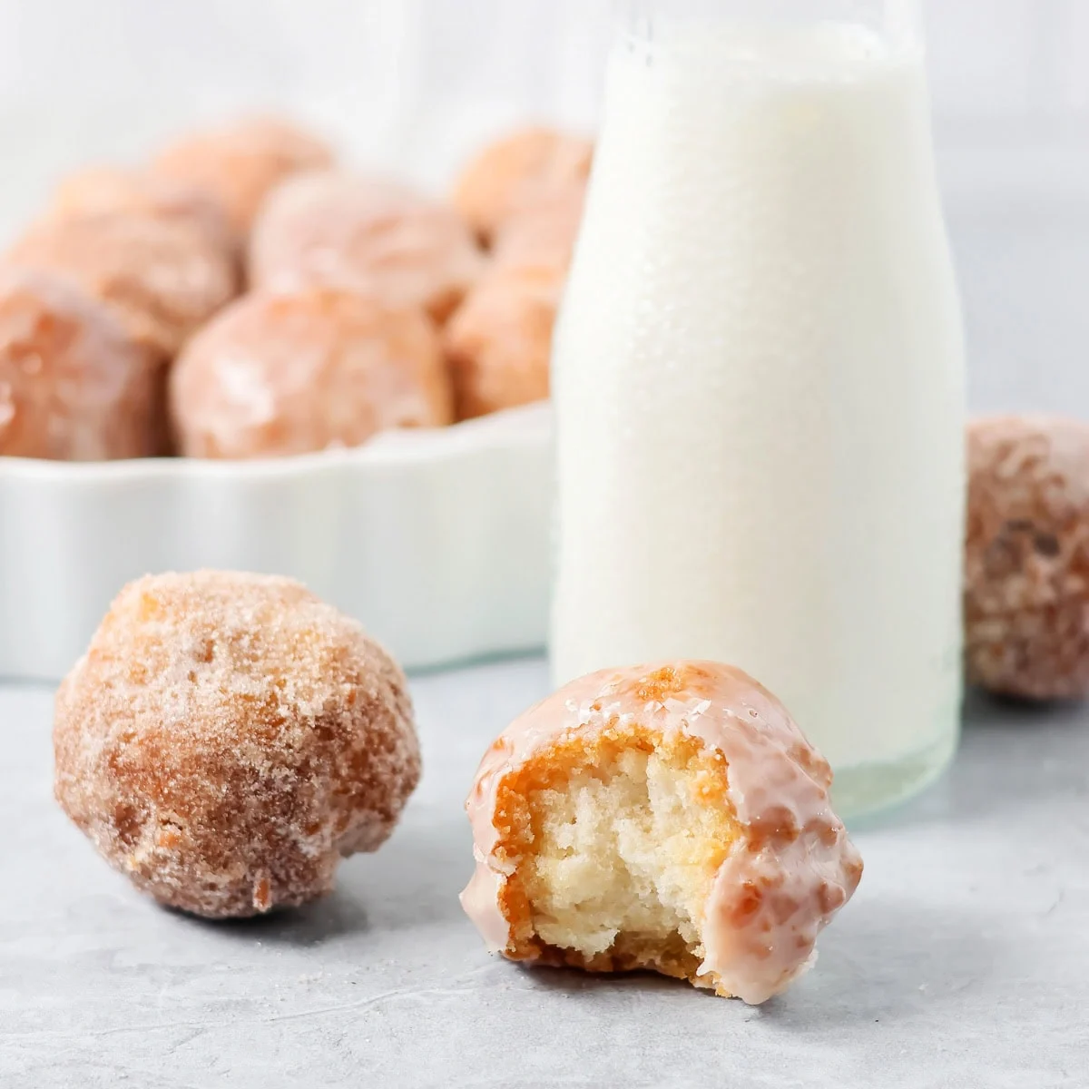 A sugared bonut and glazed bonut, with a bite taken out of it, next to a bottle of cold milk. 