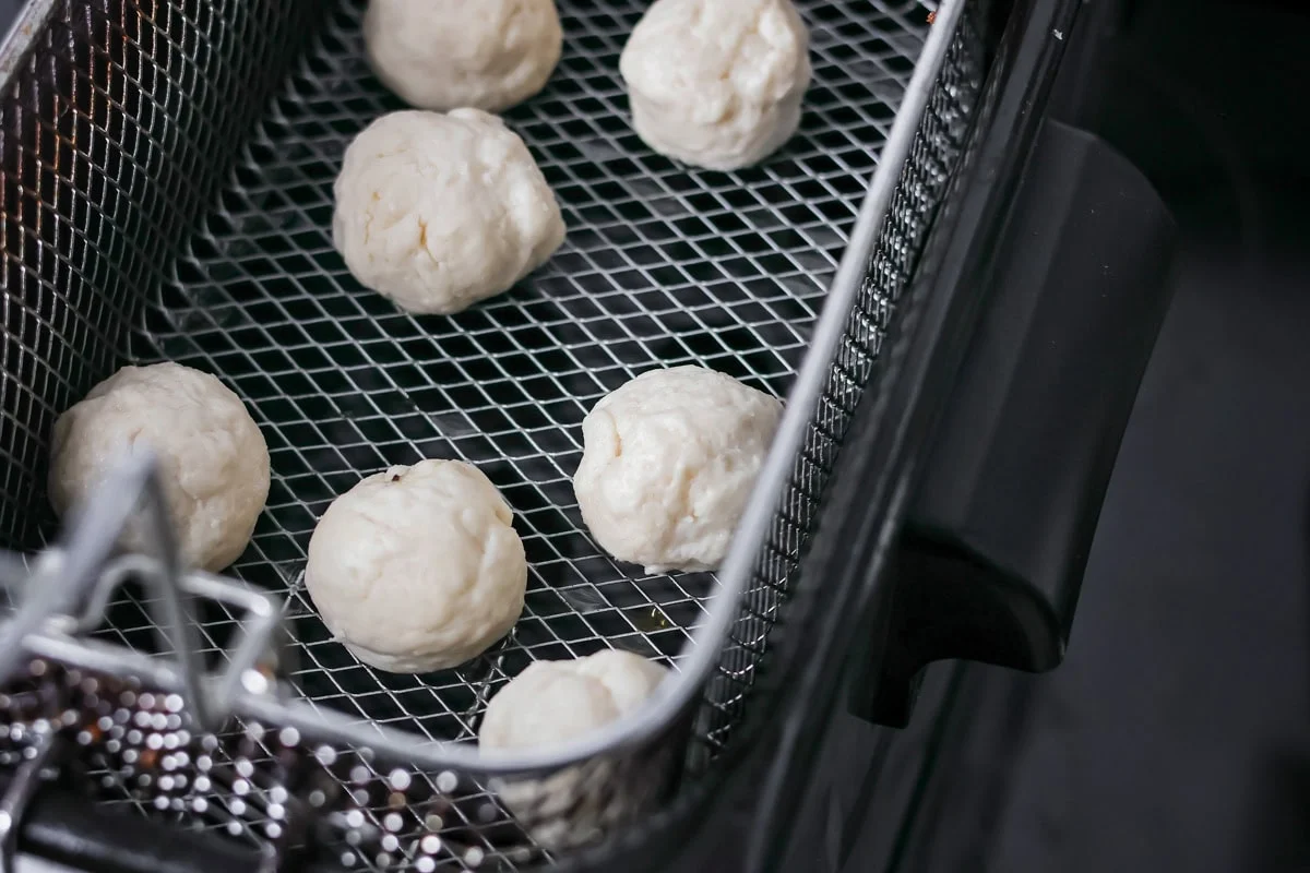Individual bonut dough balls in a deep fry basket.
