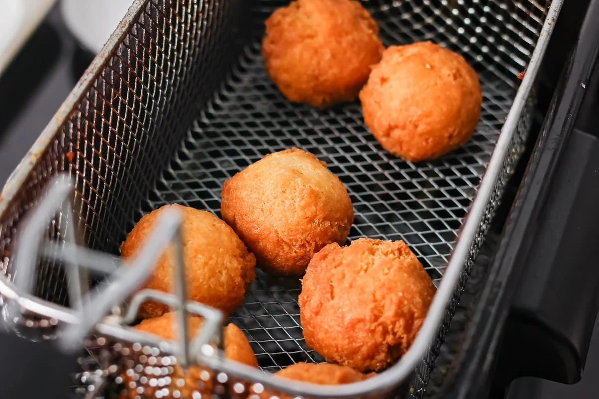 Golden brown fried bonuts in a fry basket above oil.