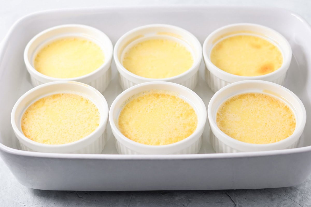 A baking dish with 6 cooked creme brulees with lightly browned tops. 