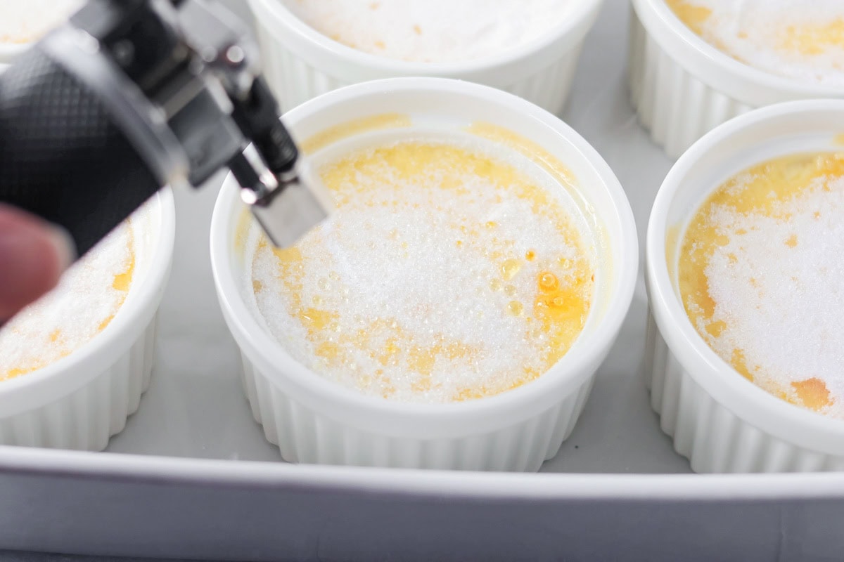 Using a kitchen torch to brown the granulated sugar on top of the creme brulees.