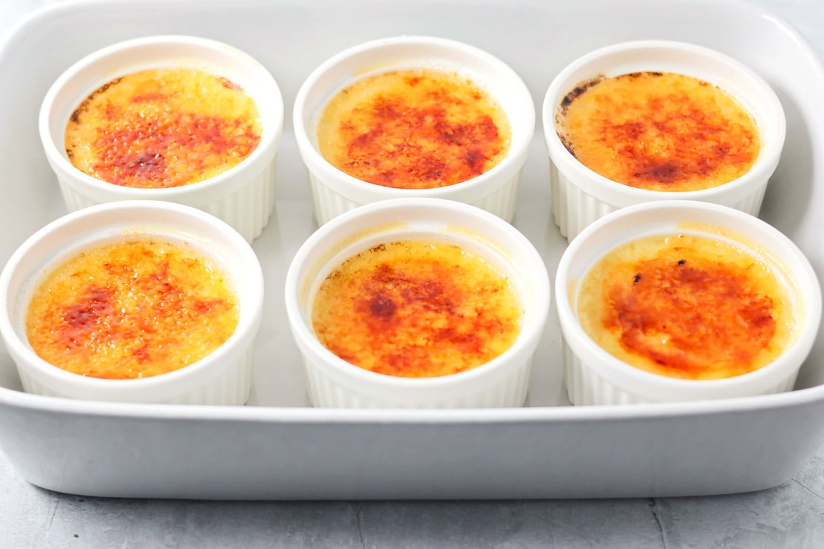 Six baked creme brulees with caramelized sugar on top.