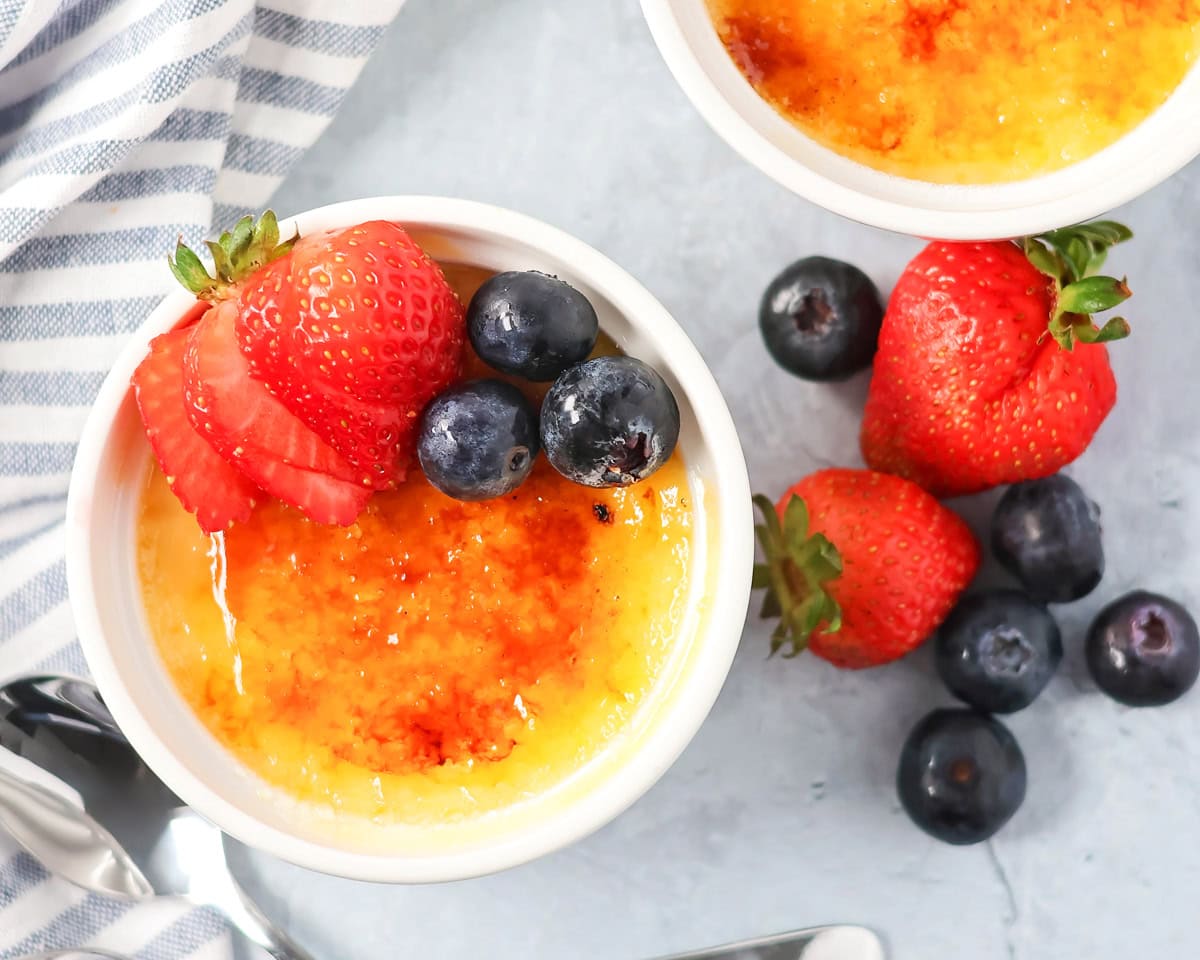 A serving of creme brulee topped with berries on a counter with extra berries on the side.