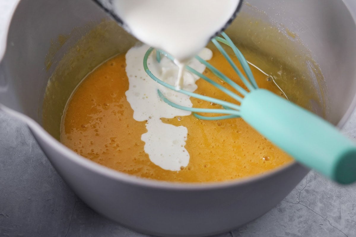 Pouring cream into a mixing bowl of egg yolk mixture.