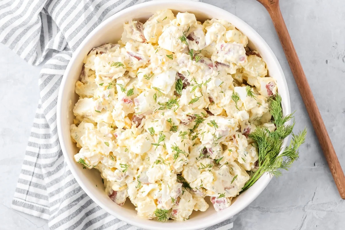Creamy potato salad in a white serving bowl garnished with fresh dill.