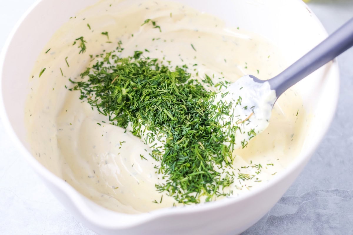 A creamy mayonnaise mixture in a mixing bowl topped with chopped dill.