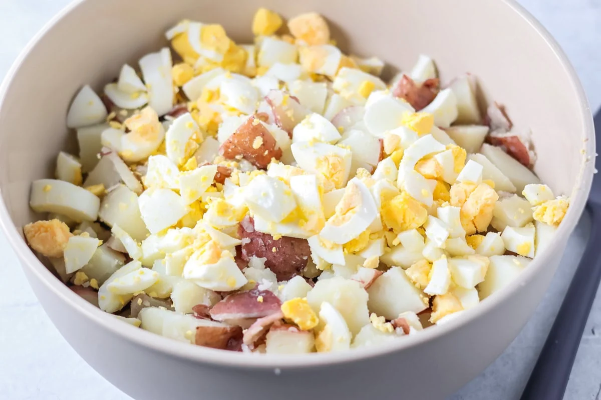 Cubed red potatoes and diced hard boiled eggs in a white mixing bowl.