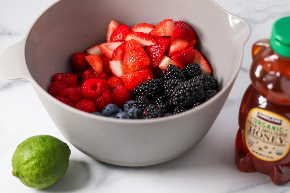 Berries, honey, and a lime on a kitchen counter.