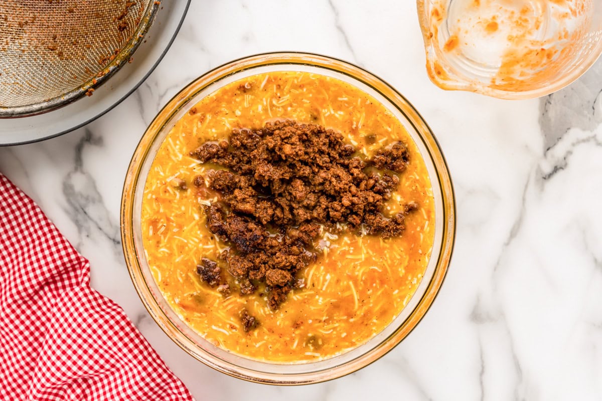Cooked chorizo added to the savory custard in a glass bowl. 