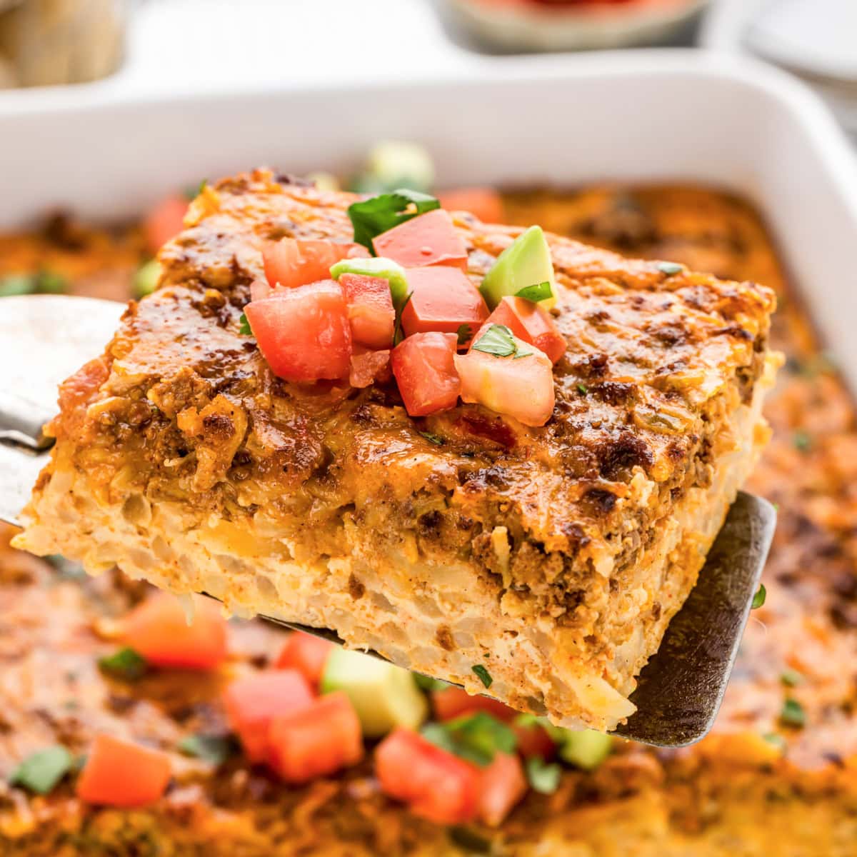 Lifting a slice of Mexican breakfast casserole out of the baking dish with a spatula.