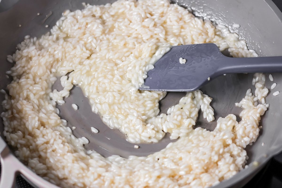 Stirring broth with the rice in a skillet to create a creamy texture.