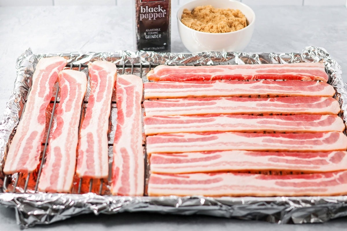 This 3-ingredient candied bacon is the perfect balance of sweet and salty and the ultimate upgrade to any gathering. Thick cut bacon strips set out on a wire rack set above a foil lined pan.