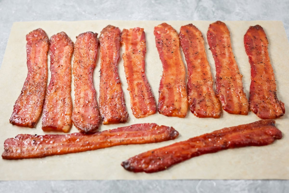 This 3-ingredient candied bacon is the perfect balance of sweet and salty and the ultimate upgrade to any gathering. Candied bacon strips cooling on a pice of parchment paper.