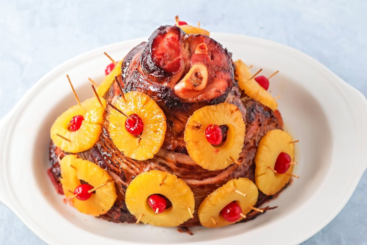 A fully baked Christmas ham on a white serving platter; it looks like a Christmas tree.
