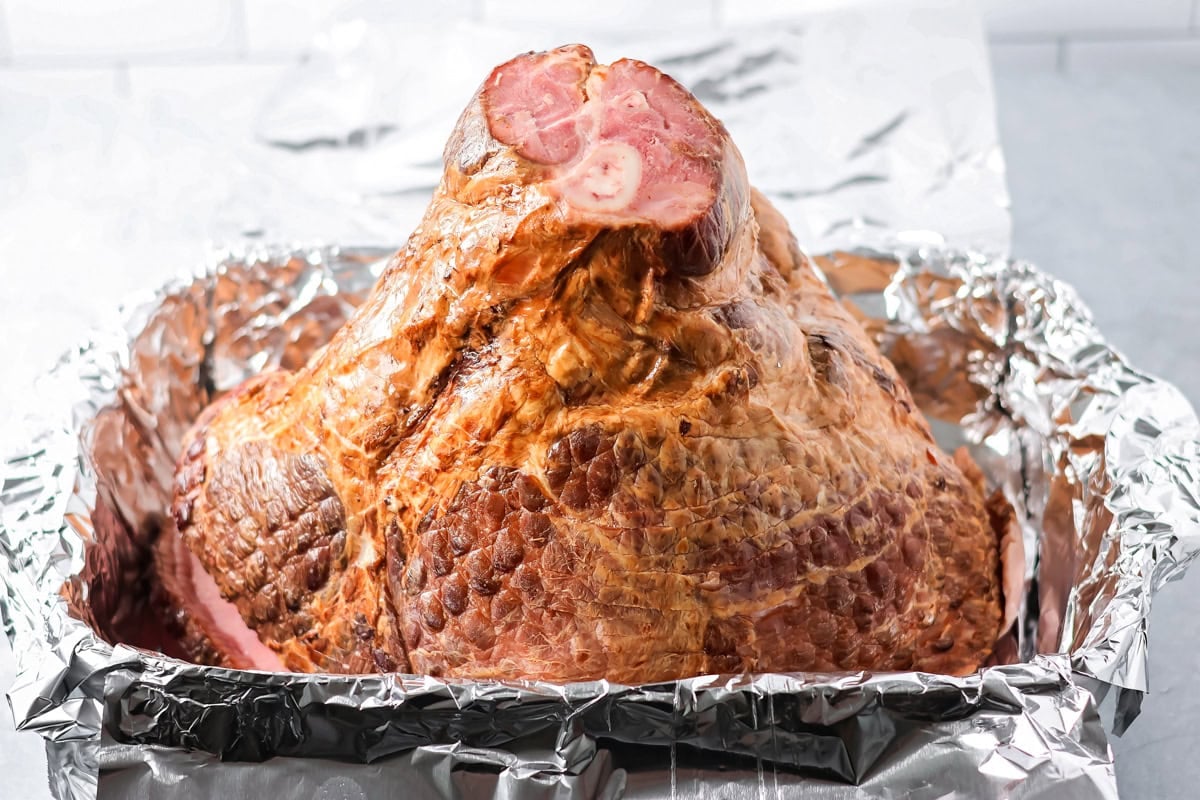 A spiral cut ham sitting with the large end against the aluminum lined pan and the short end facing up. 