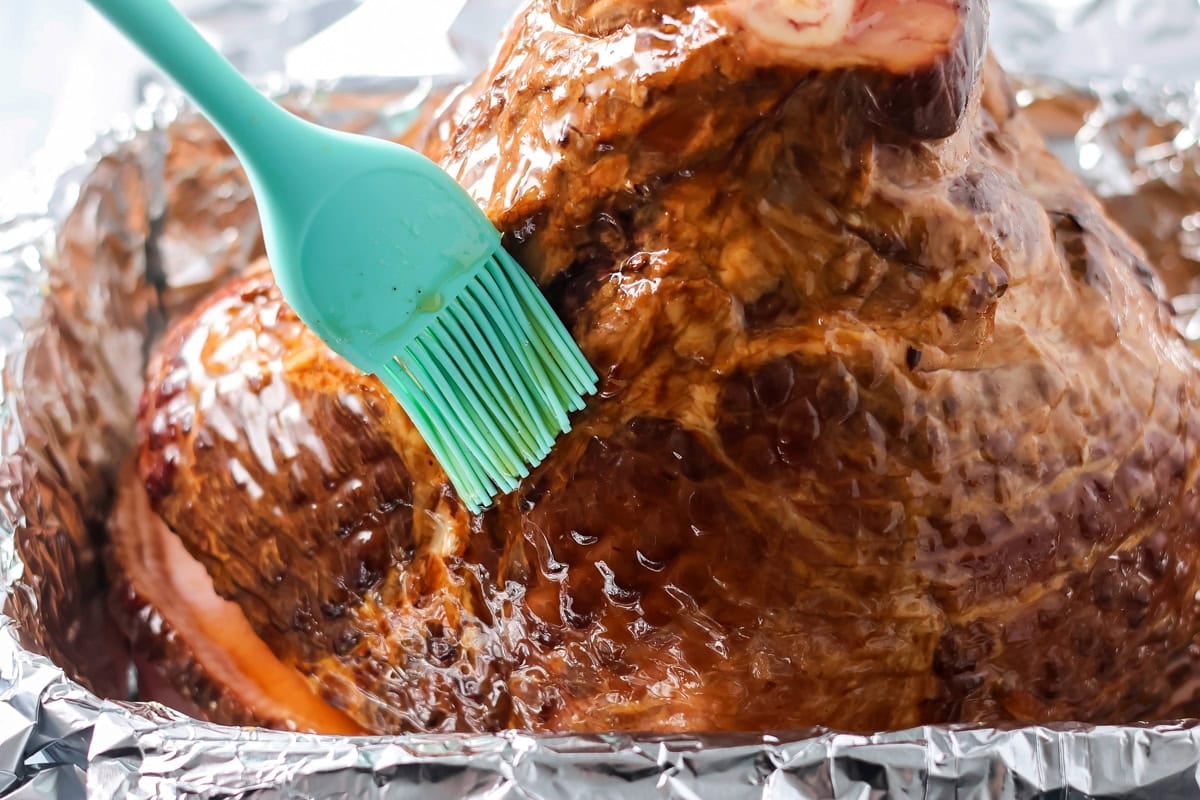 Basting the glaze all over the ham.