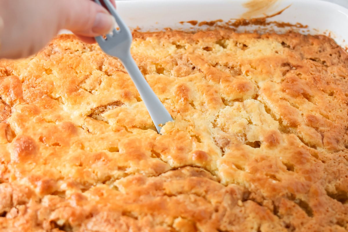 Using the flat end of a fork to poke holes into a baked cinnamon roll cake.