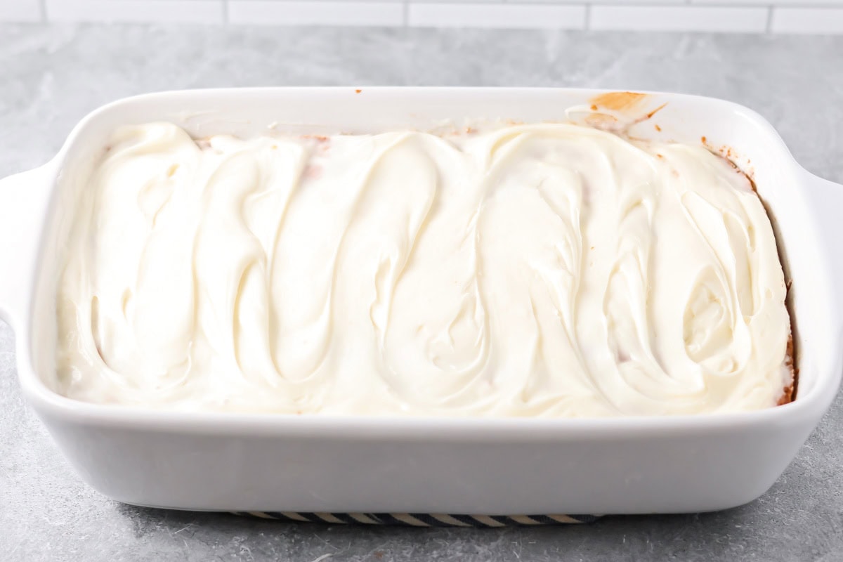 Cream cheese frosting spread over the top of a cinnamon roll poke cake.