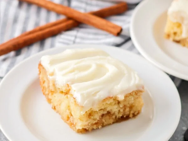 Slice of cinnamon roll poke cake served on a white plate.