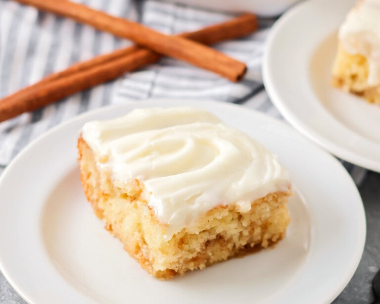 Slice of cinnamon roll poke cake served on a white plate.
