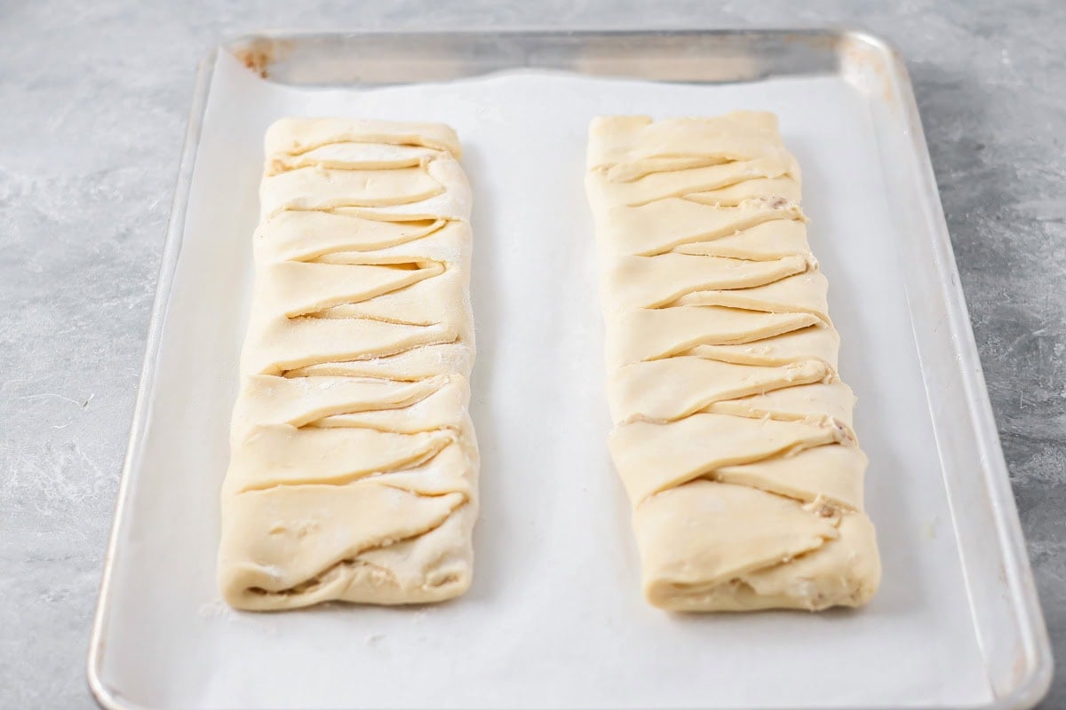 A pair of unbaked folded Danish kringles on a baking pan.