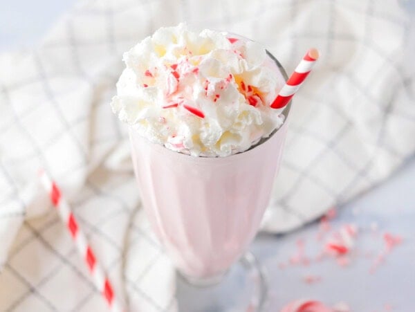 Peppermint milkshake served in a glass and topped with whipped cream and crushed candy canes.