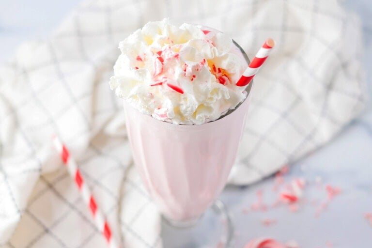 Peppermint milkshake served in a glass and topped with whipped cream and crushed candy canes.