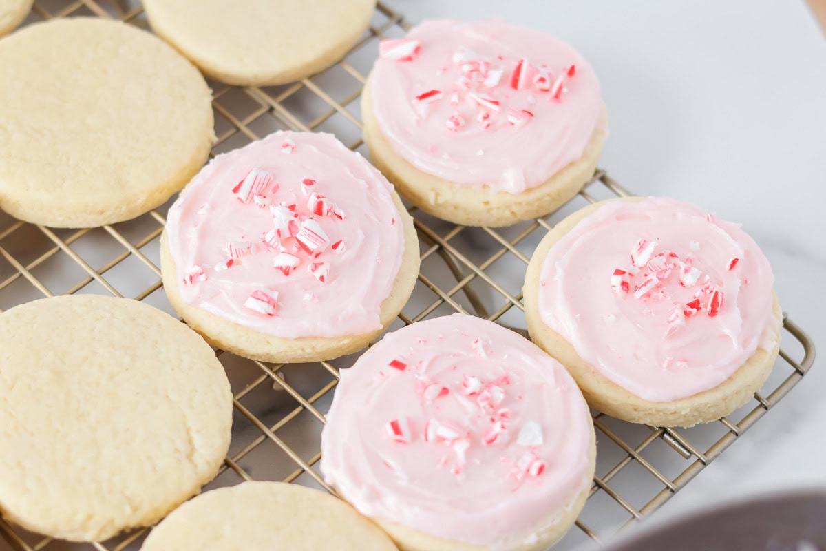 Four pink frosted sugar cookies with peppermint candy sprinkles on top and plain sugar cookies.