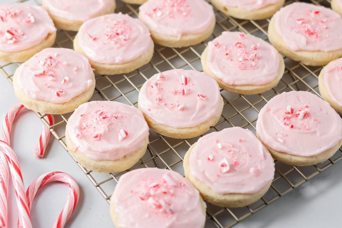 A cooling rack full of pink frosted sugar cookies with peppermint candy sprinkles on top.