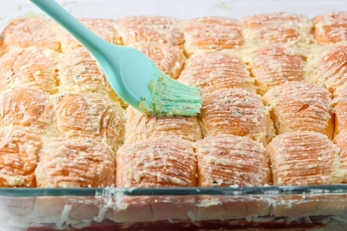 Brushing flavored melted butter on top of the Hawaiian sweet rolls.