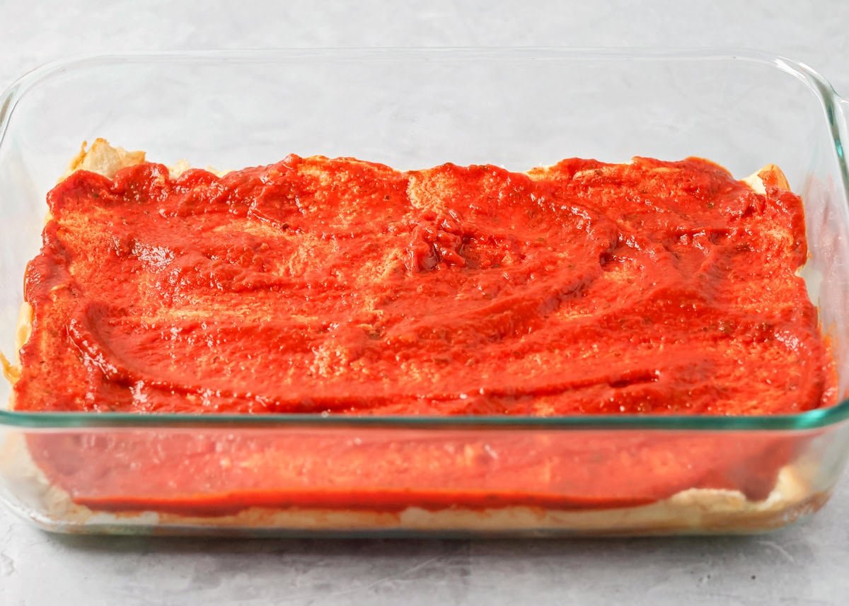 The bottom layer of Hawaiian sweet roll in a glass baking dish topped with pizza sauce.