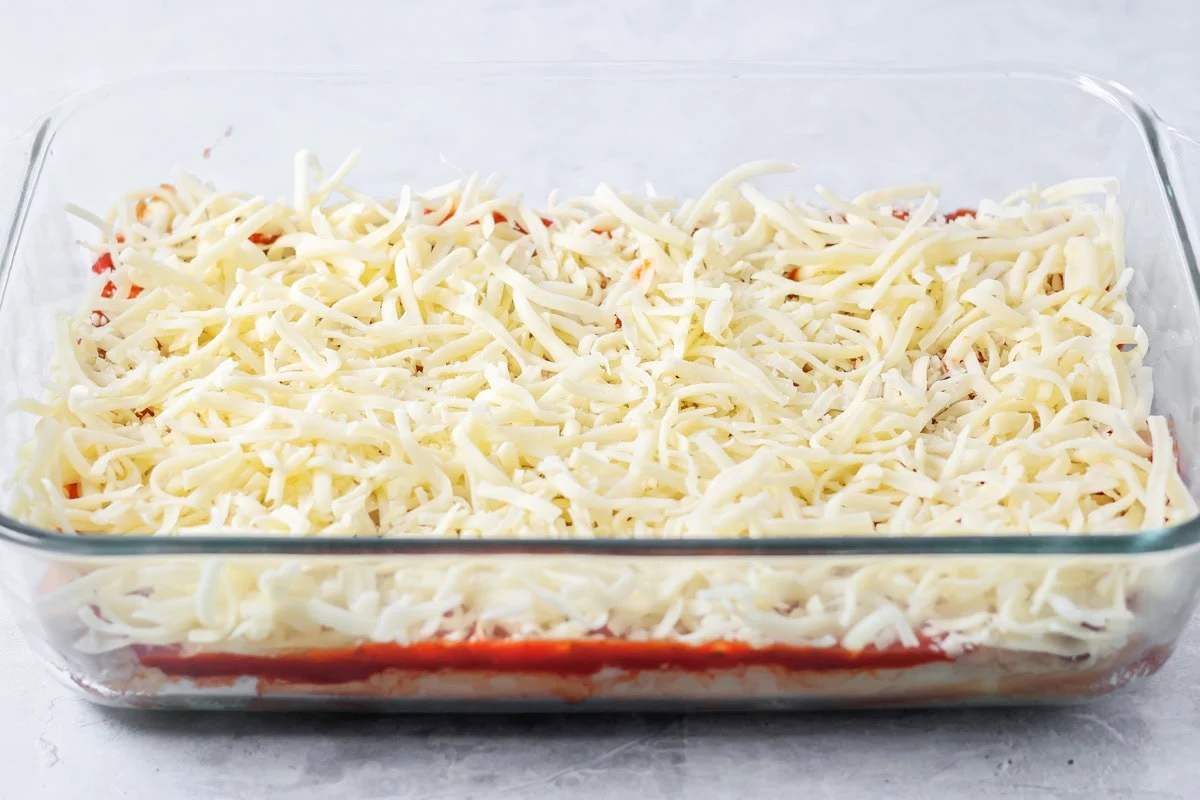 A layer of shredded cheese added to the pizza slider recipe in glass baking dish.