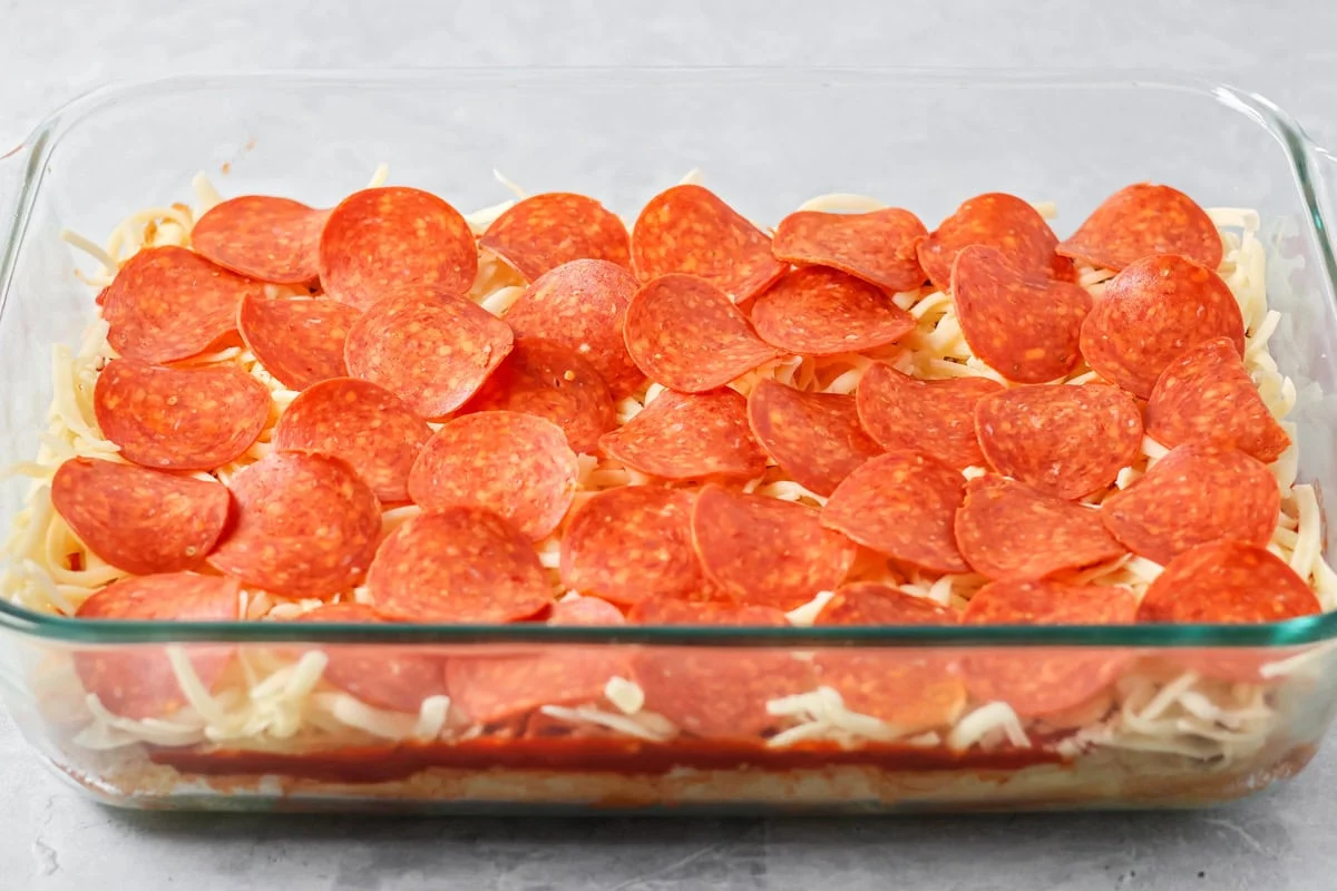 A layer of pepperoni added to the pizza slider recipe in glass baking dish.