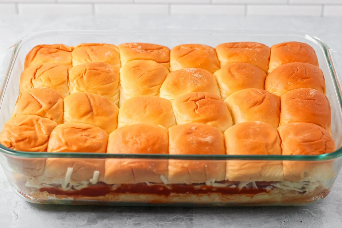 The top block of Hawaiian sweet rolls added to the pizza slider recipe in glass baking dish.