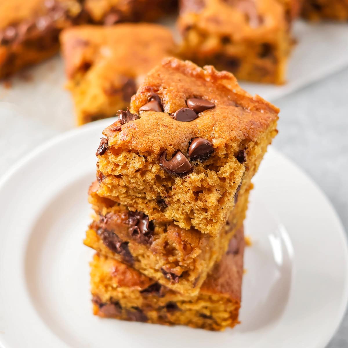 Three slices of pumpkin chocolate chip bars stacked on a white plate.