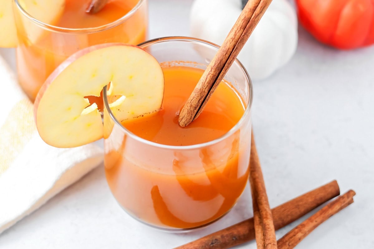 Pumpkin juice, the iconic wizarding world beverage, can be served chilled or heated for a bit of autumn magic in every sip! A glass of pumpkin juice with a cinnamon stick in it and apple slice.