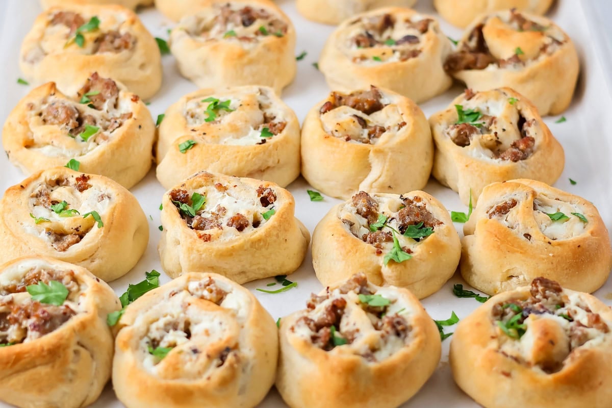 Filled with sausage crumbles and cream cheese, these sausage pinwheels are the ultimate savory snack or party appetizer! Baked sausage pinwheels on a baking sheet.