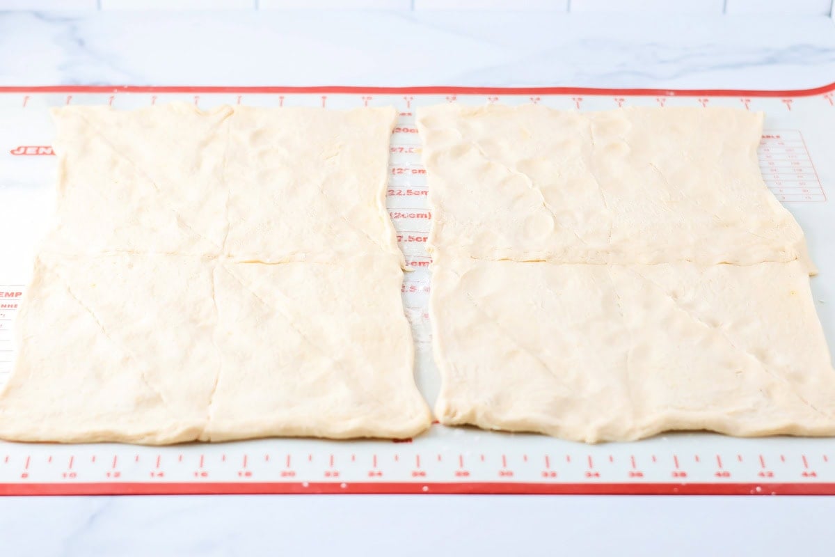 Filled with sausage crumbles and cream cheese, these sausage pinwheels are the ultimate savory snack or party appetizer! Two crescent rolls rolled on a baking mat.