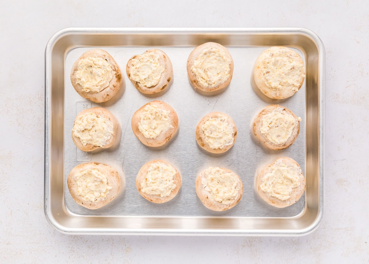 These cream cheese stuffed mushrooms are an easy, savory appetizer thatโs always the first to disappear at any party! Filled mushrooms on a baking sheet.