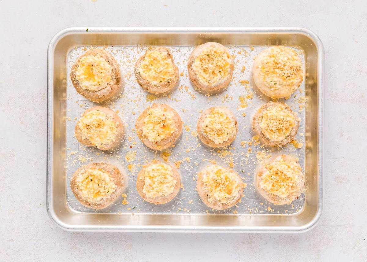 These cream cheese stuffed mushrooms are an easy, savory appetizer thatโs always the first to disappear at any party! Filled mushrooms sprinkles with parmesan cheese on a baking sheet.