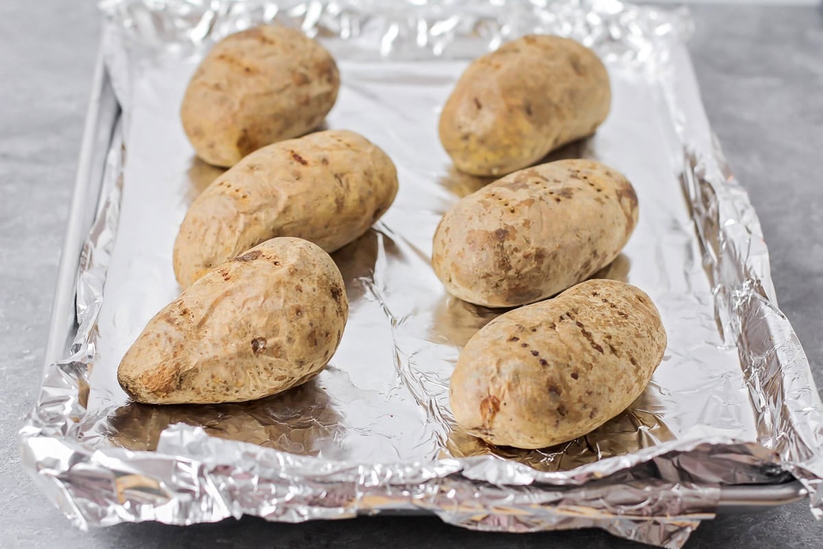 Easy twice baked potatoes are loaded with sour cream, cheese, bacon, and seasonings for the perfect savory side or main dish! Baked potatoes on a baking sheet.