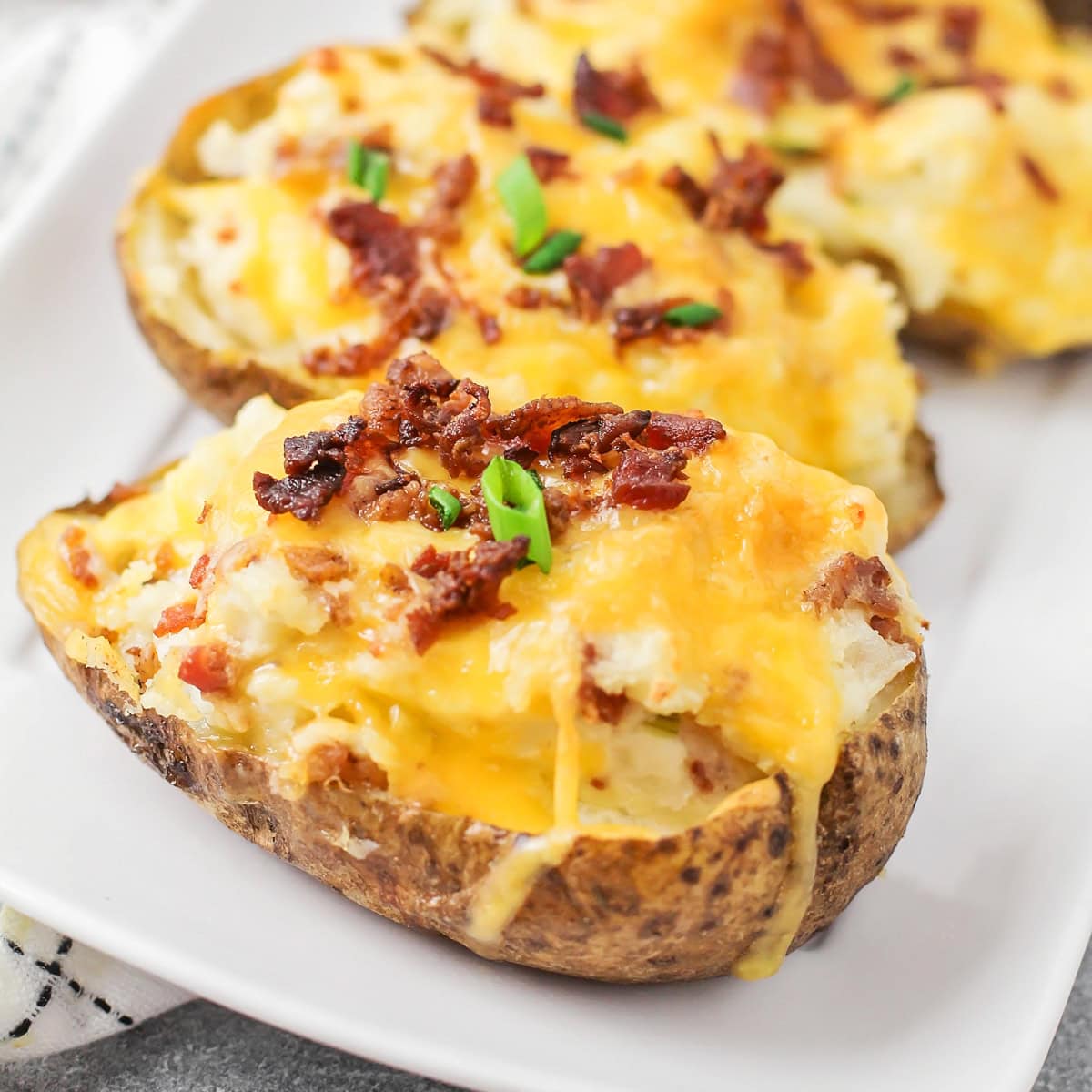 Easy twice baked potatoes are loaded with sour cream, cheese, bacon, and seasonings for the perfect savory side or main dish! Fully baked twice baked potatoes on a serving plate.